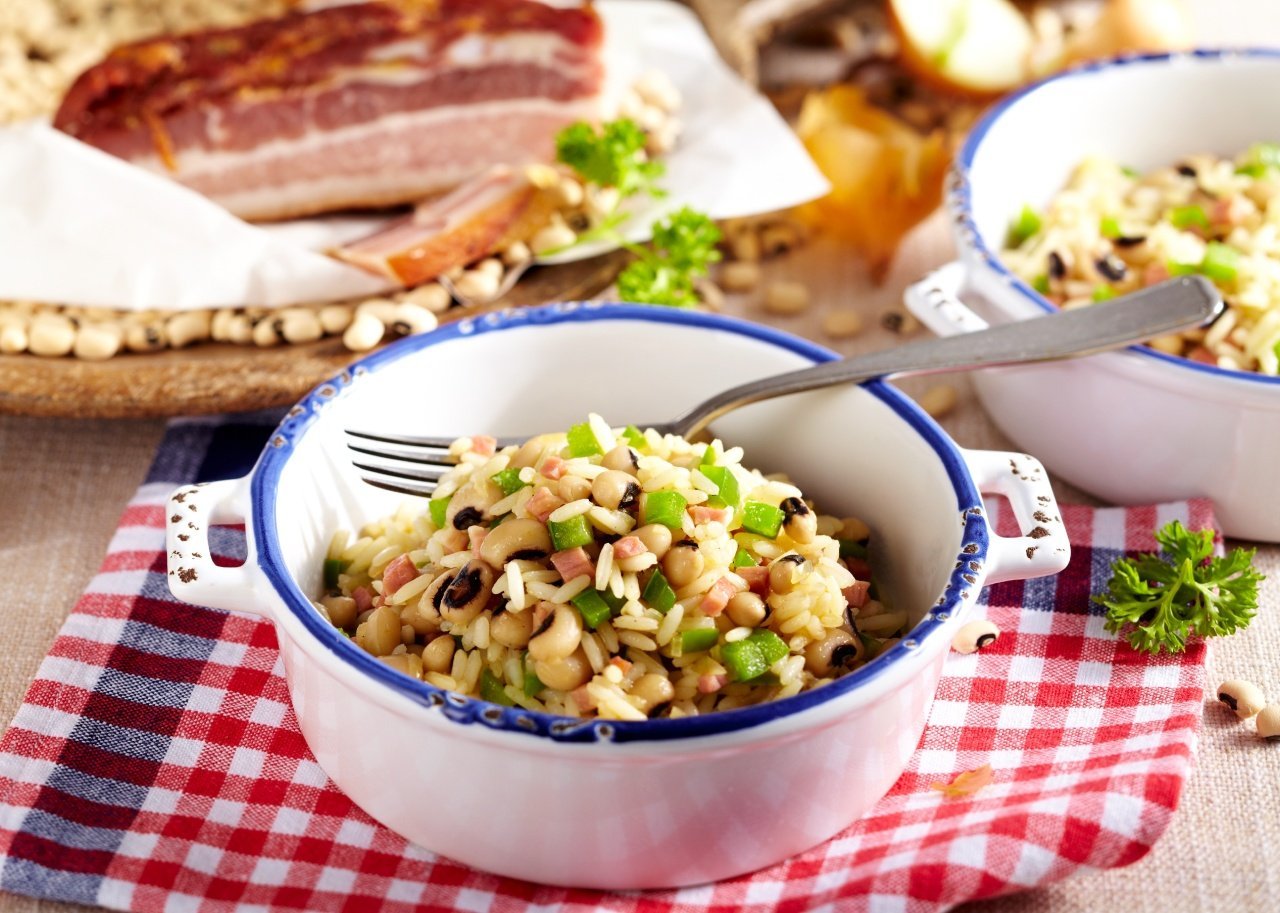 A bowl of Hoppin' John with a fork on a red checked placemat on a table with other dishes in the background.