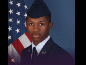 A young man in military uniform standing in front of an American flag.