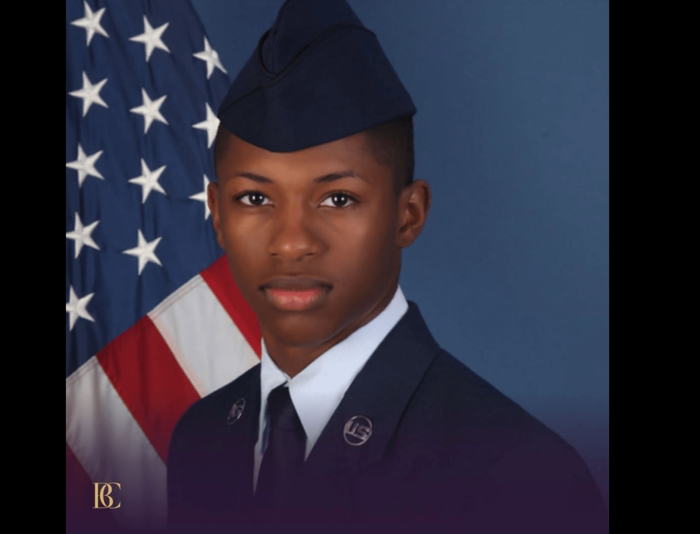 A young man in military uniform standing in front of an American flag.