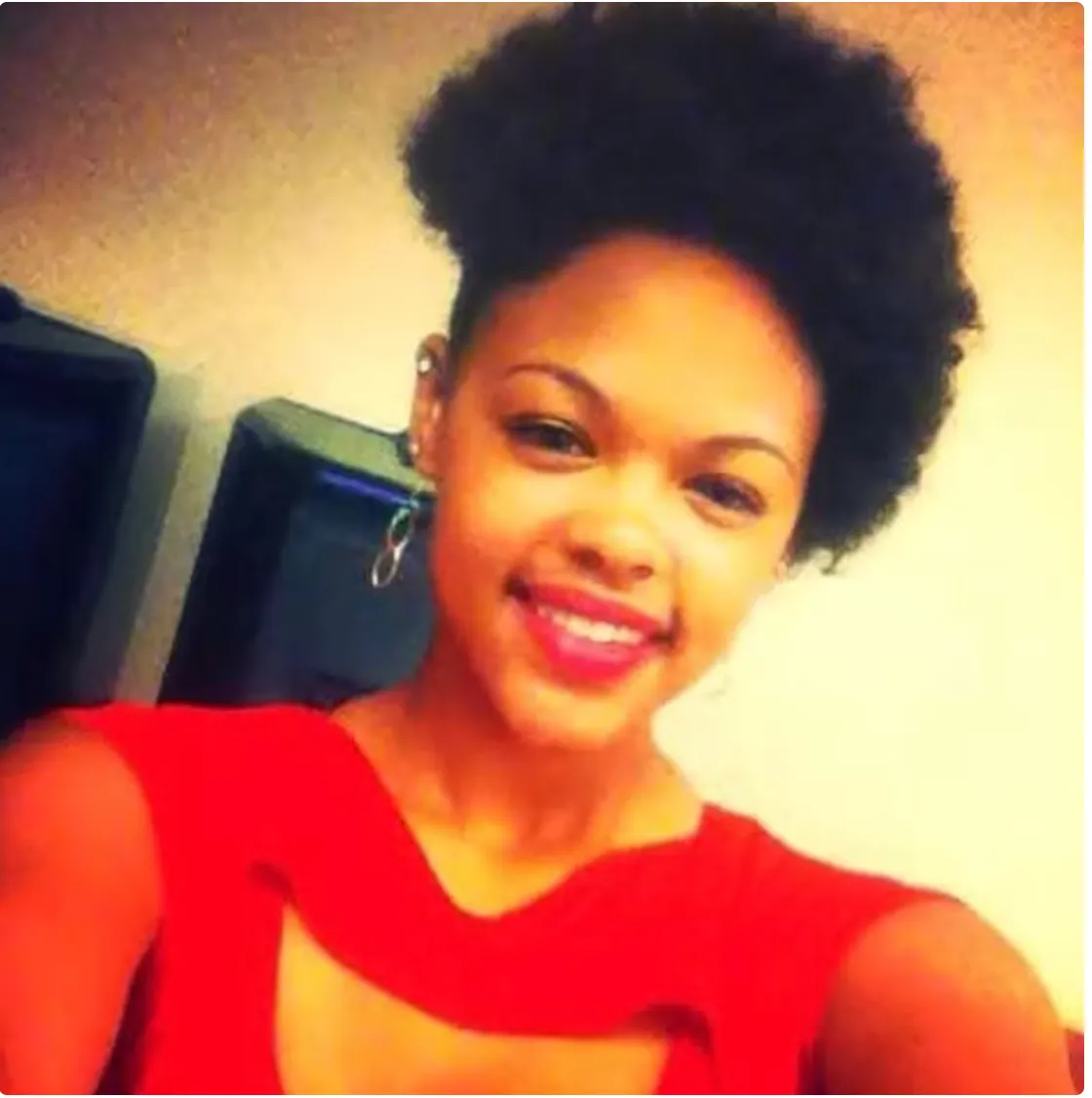A smiling woman with curly black hair wearing a red top.