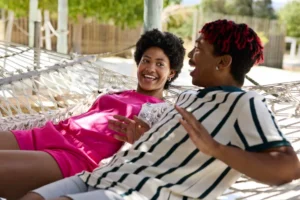 Carefree non-binary person talking with male friend on hammock