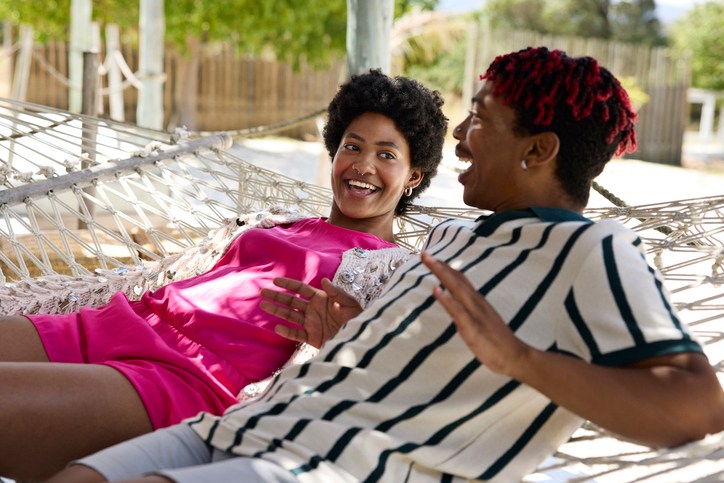 Carefree non-binary person talking with male friend on hammock
