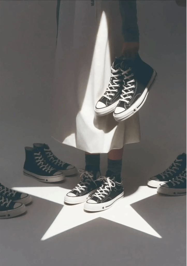 Several pairs of black Converse sneakers arranged on a white background, casting shadows in the shape of a star.