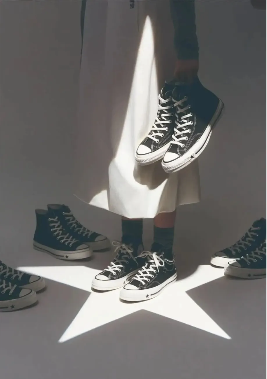 Several pairs of black Converse sneakers arranged on a white background, casting shadows in the shape of a star.