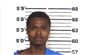 Mugshot of a man with a serious expression, wearing a blue shirt, against a height measurement backdrop.