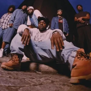 A group of five Black men in casual clothing, including a white hooded sweatshirt, standing and sitting together in an outdoor setting.