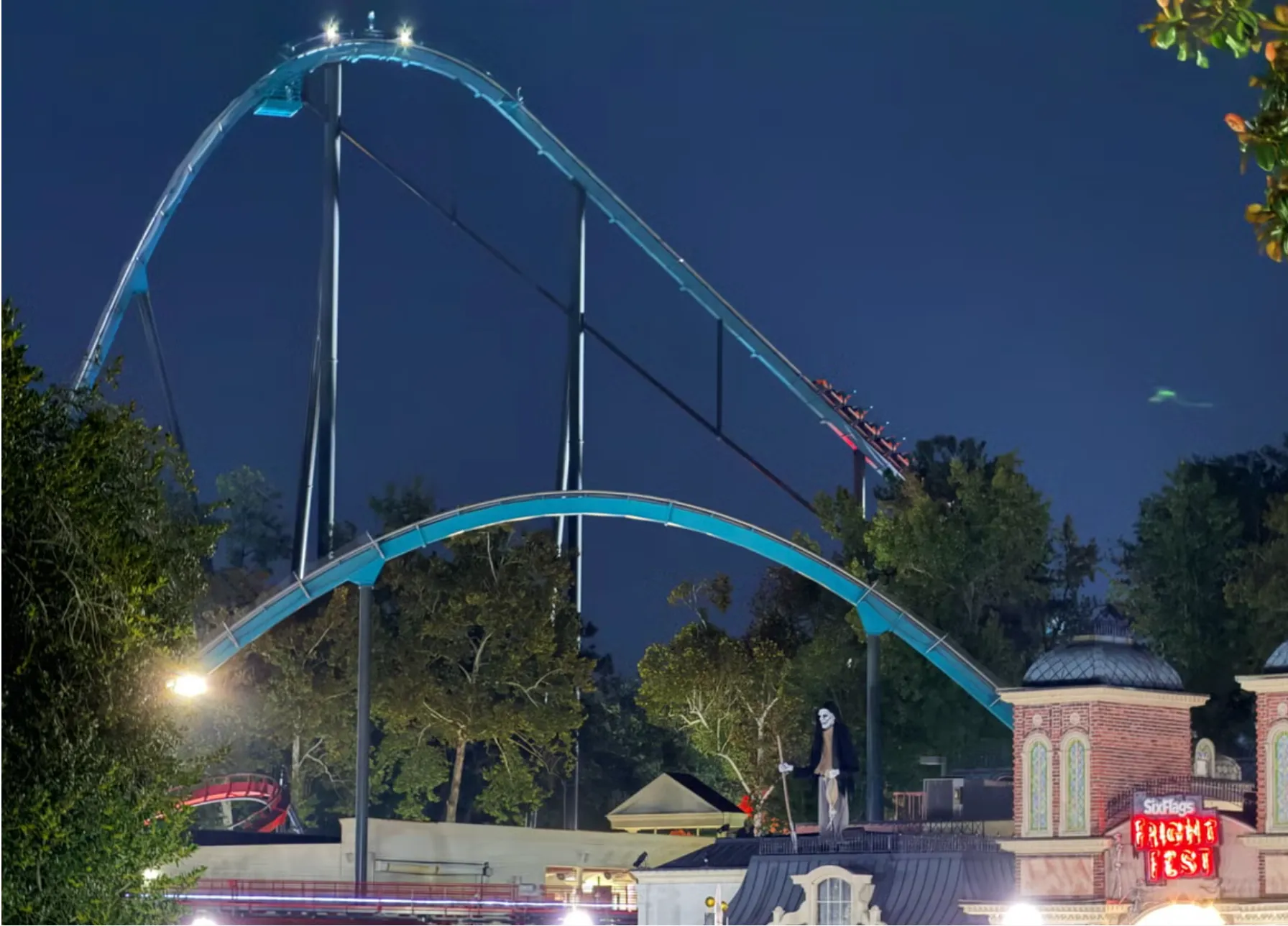 Goliath roller coaster illuminated at night at Six Flags Over Georgia, with a red train descending the steep track, surrounded by trees and park buildings with "FRIGHT FEST" signage visible.