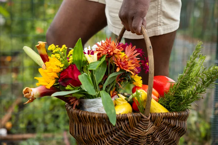 A man walking with a basket of fresh garden vegetables and flowers.